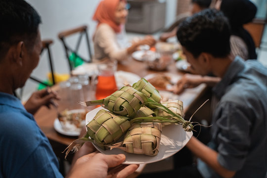 close up of ketupat with people eating dinner on the background. focus on ketupat or rice cake. eid mubarak celebration fasting