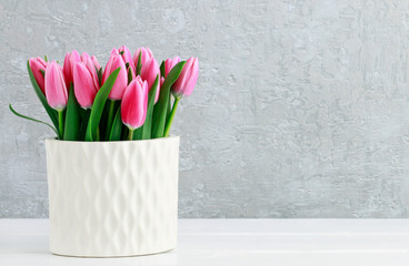 Pink tulips in white ceramic vase, grey stone background.