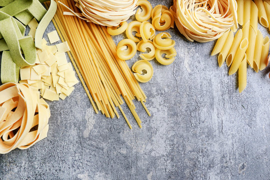 Mixed types and shapes of italian pasta on grey stone background