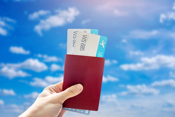 Hand holding a passport and two air tickets on a blue background of cloudy sky. Travel and vacation in beautiful places