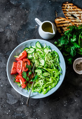 Fresh seasonal cabbage, cucumbers, peppers, tomatoes, cilantro salad and grilled bread on a dark background, top view. Healthy vegetarian diet food