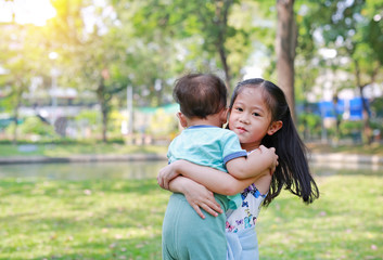 Asian sister carrying her little brother in the garden outdoor.