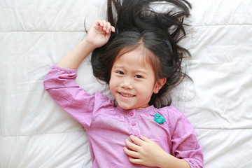 Happy little Asian child girl lying on white blanket on bed with looking at camera. Above view.