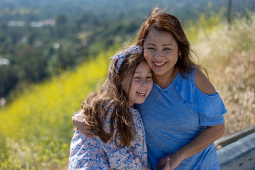 Fototapeta premium Latina Mother and Daughter Smiling and laughing on a hill in front of yellow flowers