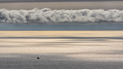 Obraz premium A wide view of the Irish Sea off the coast of Wales with silver glittering water and a small fishing boat on the sea.
