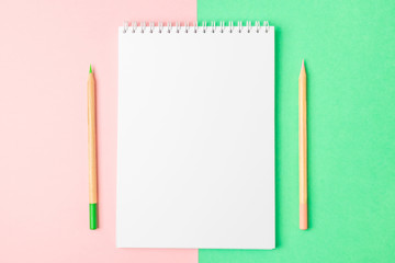 White open notebook on green and pink backgrounds. Nearby are pencils. Bright concept, flat lay, minimalism. Top view, copy space.