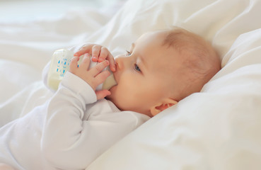 Beautiful blue-eyed child 8 months lying in bed and drinking milk from the bottle