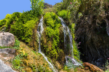 A beautiful waterfall in Spain with lots of green and blue sky photographed with long time exposure.