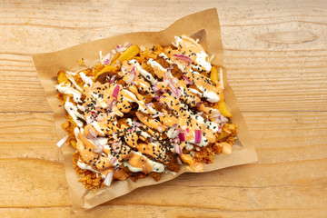 An overhead photo of an appetizing vegan dish with fried potatoes, onions, vegan cheese and soy meat, shot from the top on a rustic wooden background