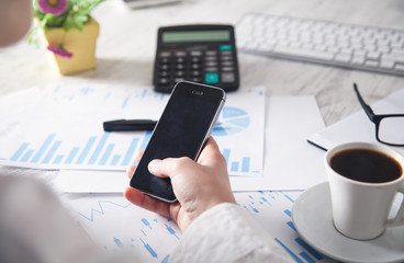 Business girl using smartphone with financial graphs in desk. Working in office