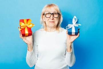 Old woman holding gifts in hand on a blue background. Mother's Day, congratulation, birthday and holiday concept.