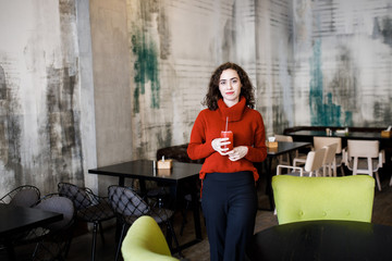 Young attractive girl sits in a cafe and drinks juice. Cozy atmosphere.