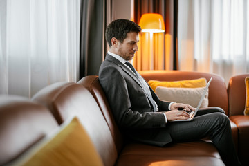 Man working on his laptop at the hotel. Executive manager typing on his laptop. Businessman sitting on the sofa working.