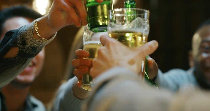 Slow motion  close up of happy young friends having fun together drinking beer and clinking glasses in a pub. Shot in 8K. Concept of friendship, holidays, celebration