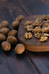 Cracked and whole walnuts lying on cutting board and wooden table, side view. Healthy nuts and seeds composition.