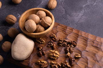 Walnuts in wooden bowl on wooden carved board, side view. Walnuts, stone and cutting board. Healthy nuts and seeds composition.