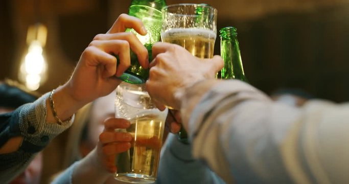 Slow motion  close up of happy young friends having fun together drinking beer and clinking glasses in a pub. Shot in 8K. Concept of friendship, holidays, celebration