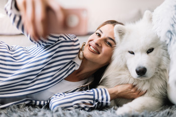 Girl taking a selfie with her dog. Pretty girl and her dog taking a selfie on the floor. Cute white dog posing for a camera shot with his owner.