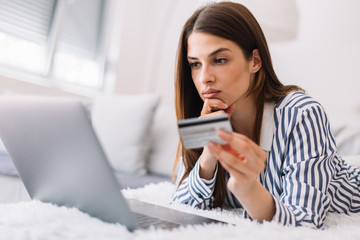 Fototapeta premium Girl is online shopping at home. Young woman holding credit card and using laptop computer. Online shopping concept