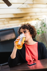 Girl having a beer while waiting for a friend. Short haired woman drinking beer at a bar.  Brunette drinks beer.
