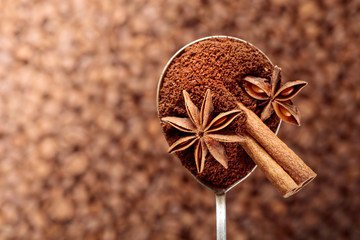 Spoon of ground coffee with anise and cinnamon on the background of coffee beans.