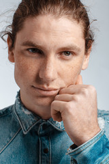 Portrait of a handsome long-haired man with drawn hair and freckles dressed in a denim shirt