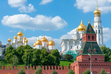 Fototapeta na wymiar Golden domes of white Orthodox churches behind the walls of the Kremlin against a bright blue sky with white clouds.