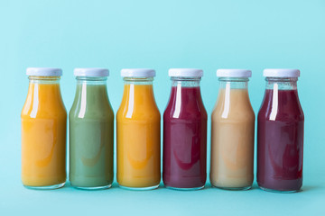 Raw vegetable and fruit juices in glass bottles on blue background