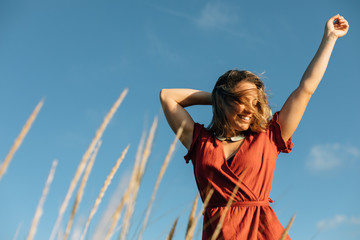 Summer freedom and relaxing leisure. Young happy woman raising arms to feel the breeze at the beach.