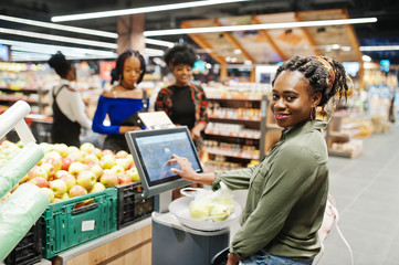 Group of african womans weighs apples in polyethylene bags at supermarket.