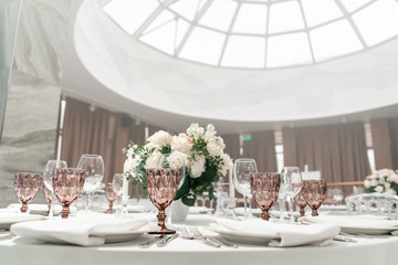 Wine glasses on round Banquet table served. Interior of restaurant for wedding dinner, ready for guests. Decorated with floral arrangement. Dishes, wine glasses and napkins. Catering concept.