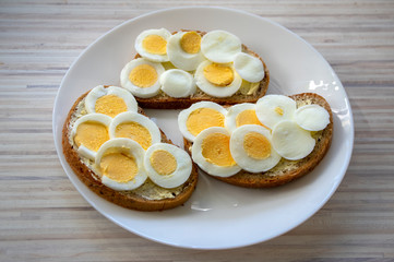 Sliced hard boiled eggs on common czech bread with butter on white plate on light wooden table