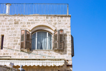 Jewish building ancient architecture in Jaffa old city near Tel Aviv light coral color brick house corner with open shutters window, blue sky background, copy space  
