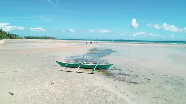 Aerial drone view of traditional philippines fishboat aground on sandy shore at El Nido, Philippines. Tropical paradise turquoise beach with palm trees and bungalow.