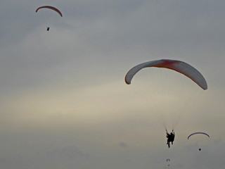 Paragliders in silhouette on a cloudy day
