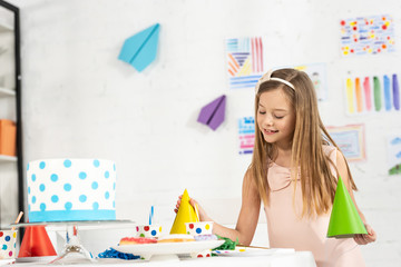 adorable smiling kid at festive table with party caps and birthday cake
