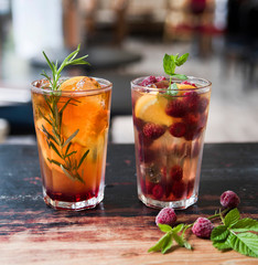 Tea in glasses on the old table against the background of a cafe and vintage teapot. Sai with orange and rosemary and tea with lemon, raspberry and mint