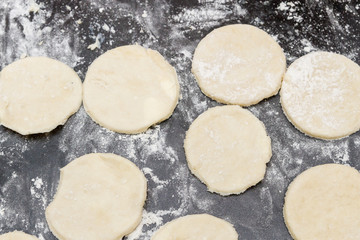 Rolled out raw dough cut into roundels on a table with scattered flour