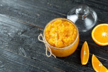 Orange homemade jam or scrub on a dark wooden table in a glass jar