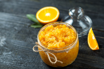 Orange homemade jam or scrub on a dark wooden table in a glass jar