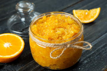 Orange homemade jam or scrub on a dark wooden table in a glass jar