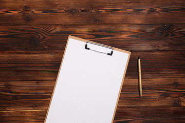 Fototapeta premium Clipboard with white sheet on wood background. Top view.