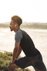 Handsome young african strong sports man listening music with earphones outdoors make exercises.
