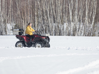 A winter forest. A young woman in bright yellow jacket riding snowmobile