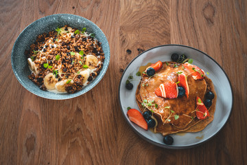 Bright plate with a healthy summer Breakfast American pancakes with berries and a power bowl made of natural yogurt cereal and banana on a wooden background