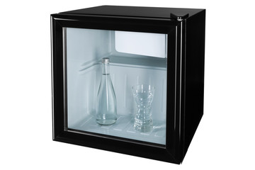 in a black mini bar or fridge with a glass door there is a glass bottle with water and a glass full...