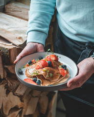 Healthy summer breakfast: delicious american pancakes with fresh strawberries and blueberries and honey carried on a plate by a waitress