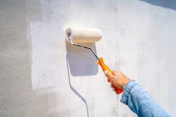 female hand painting wall with paint roller