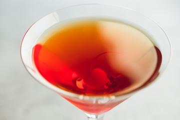 Manhattan cocktail with bourbon and maraschino cherry garnish on a white table.