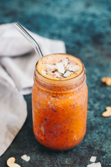 Orange fruit smoothie is made from blueberry, sea buckthorn, coconut cream, nuts and chia on a blue background. The concept of healthy summer food and drink.